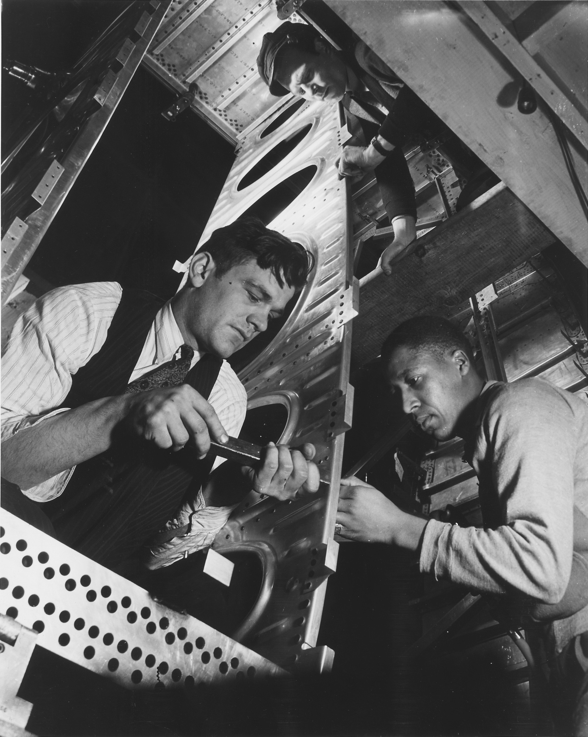 Three workers fastening metal components inside an aircraft frame at a bomber production plant, circa May 1942.