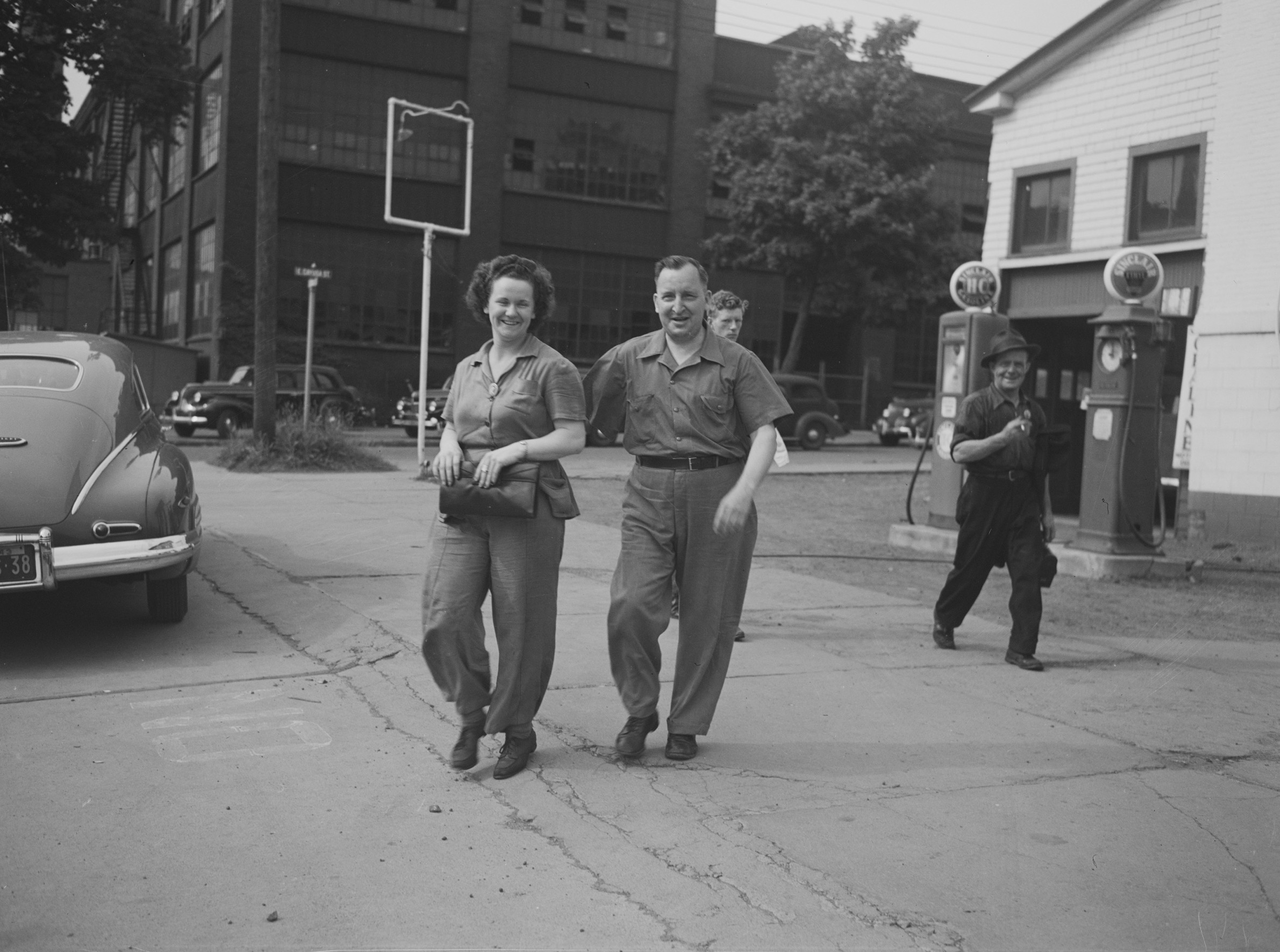 A woman and man in factory work clothes walking away from an industrial plant at the end of a shift in Oswego, New York, in June 1943.