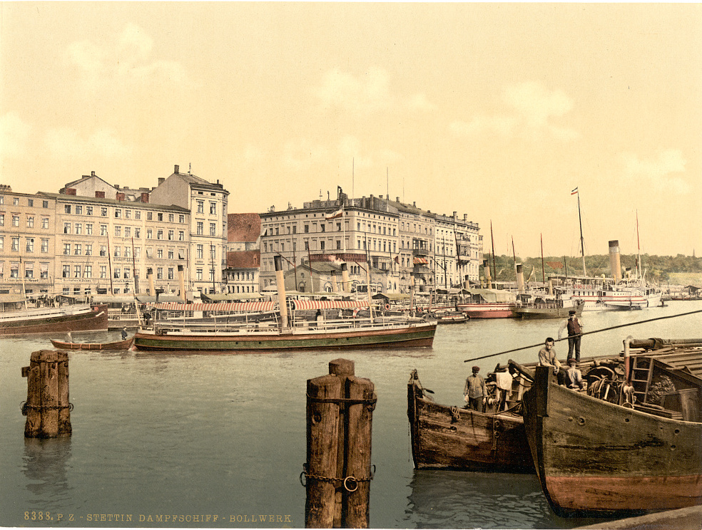 Historic color view of a European steamship wharf with vessels, warehouses, and waterfront traffic